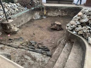 backyard-excavation Wide shot of a backyard excavation project with piles of demolished concrete and dirt being staged for removal.
