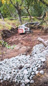 bobcat-land-clearing A Bobcat skid steer clearing brush and leveling dirt on a wooded residential lot for new construction prep.