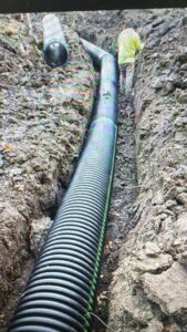 drain-pipe-install High-capacity black corrugated drainage pipe being installed in a deep trench for residential storm water management.