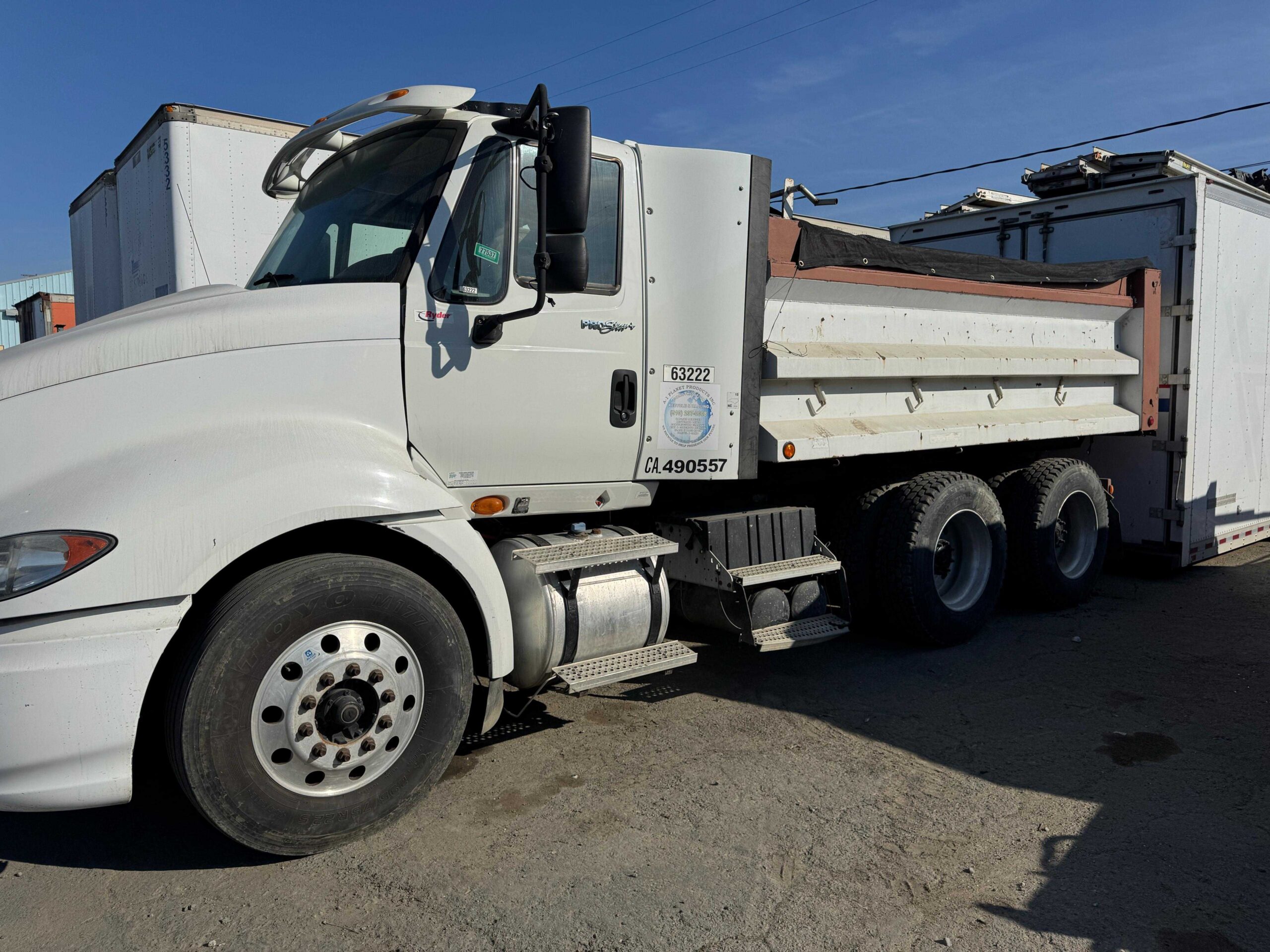 Bulk Aggregates and Soil Delivery Truck White heavy-duty tandem-axle dump truck parked alongside a large commercial transport trailer.
