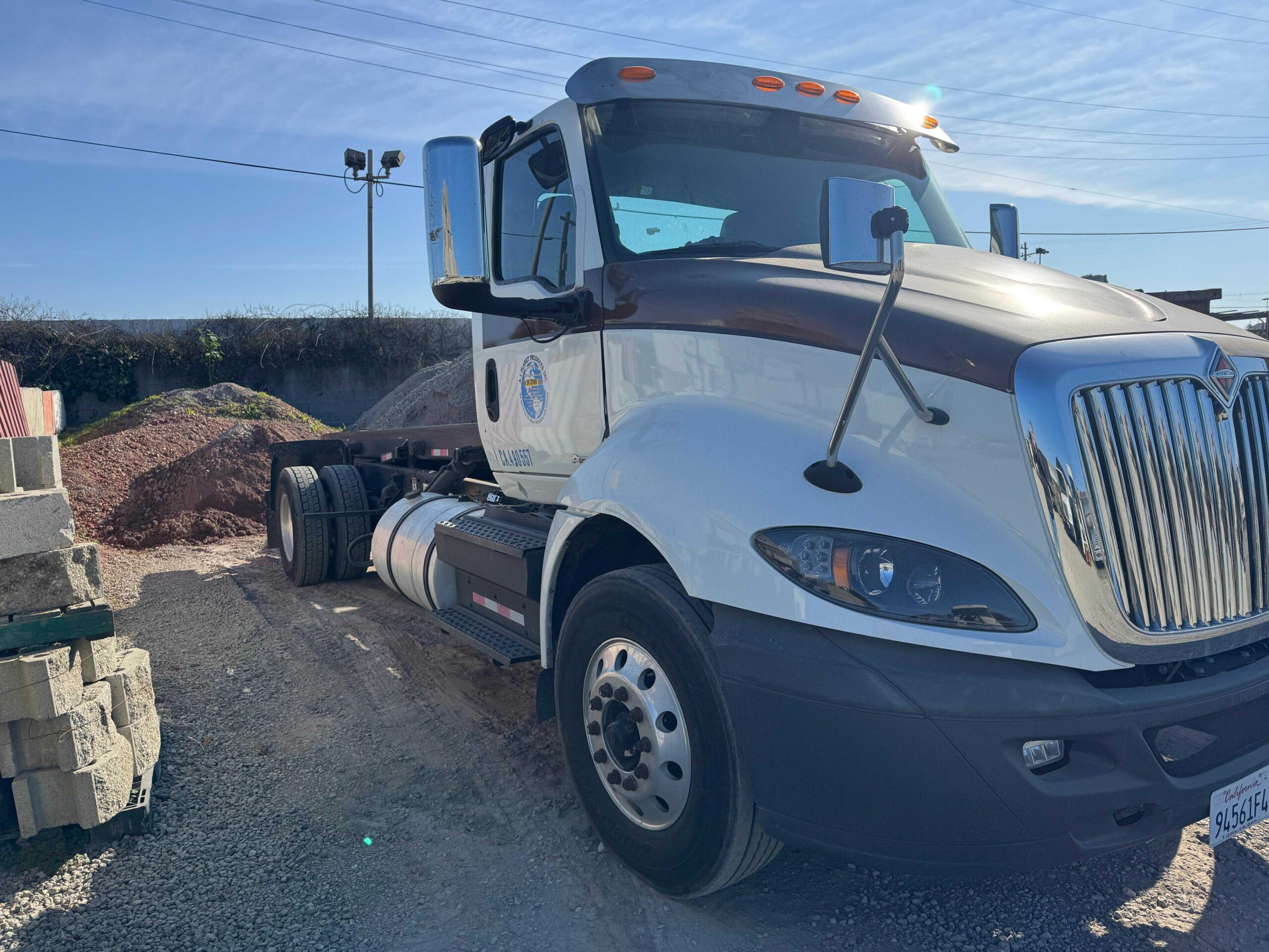 Commercial Hauling Infrastructure Lineup of commercial dump trucks, flatbeds, and hauling vehicles parked in a gravel lot under a clear blue sky.