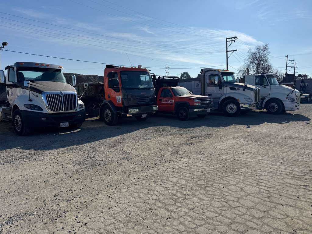 Full Service Commercial Hauling Fleet White and maroon commercial dump truck chassis parked next to building materials and gravel piles.