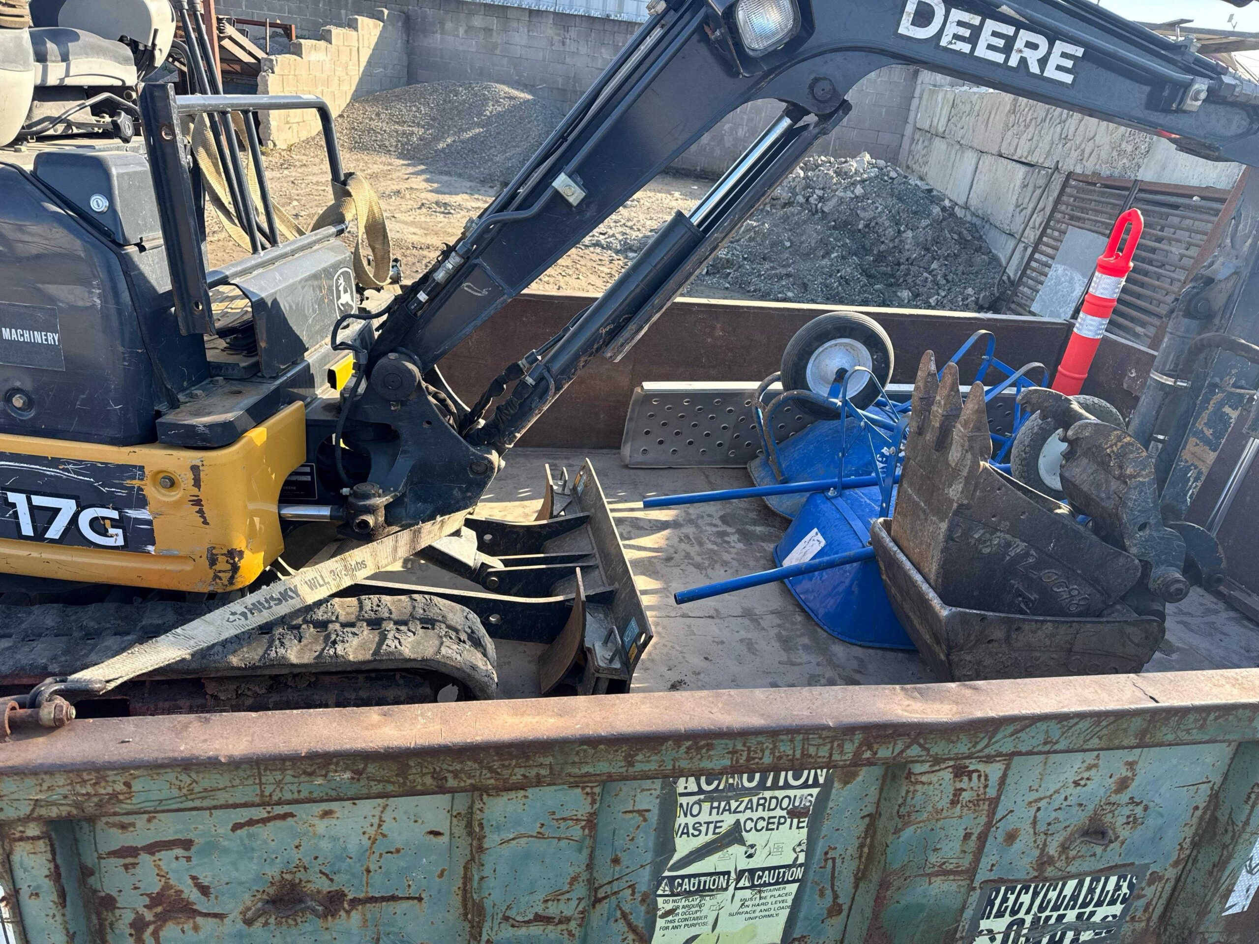 Ready to Excavate and Clean Up Yellow John Deere mini excavator packed securely into a truck bed alongside blue wheelbarrows and construction tools.